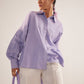 Stylera Era purple oversized cotton shirt with ruched sleeves worn with white pants and purple handbag