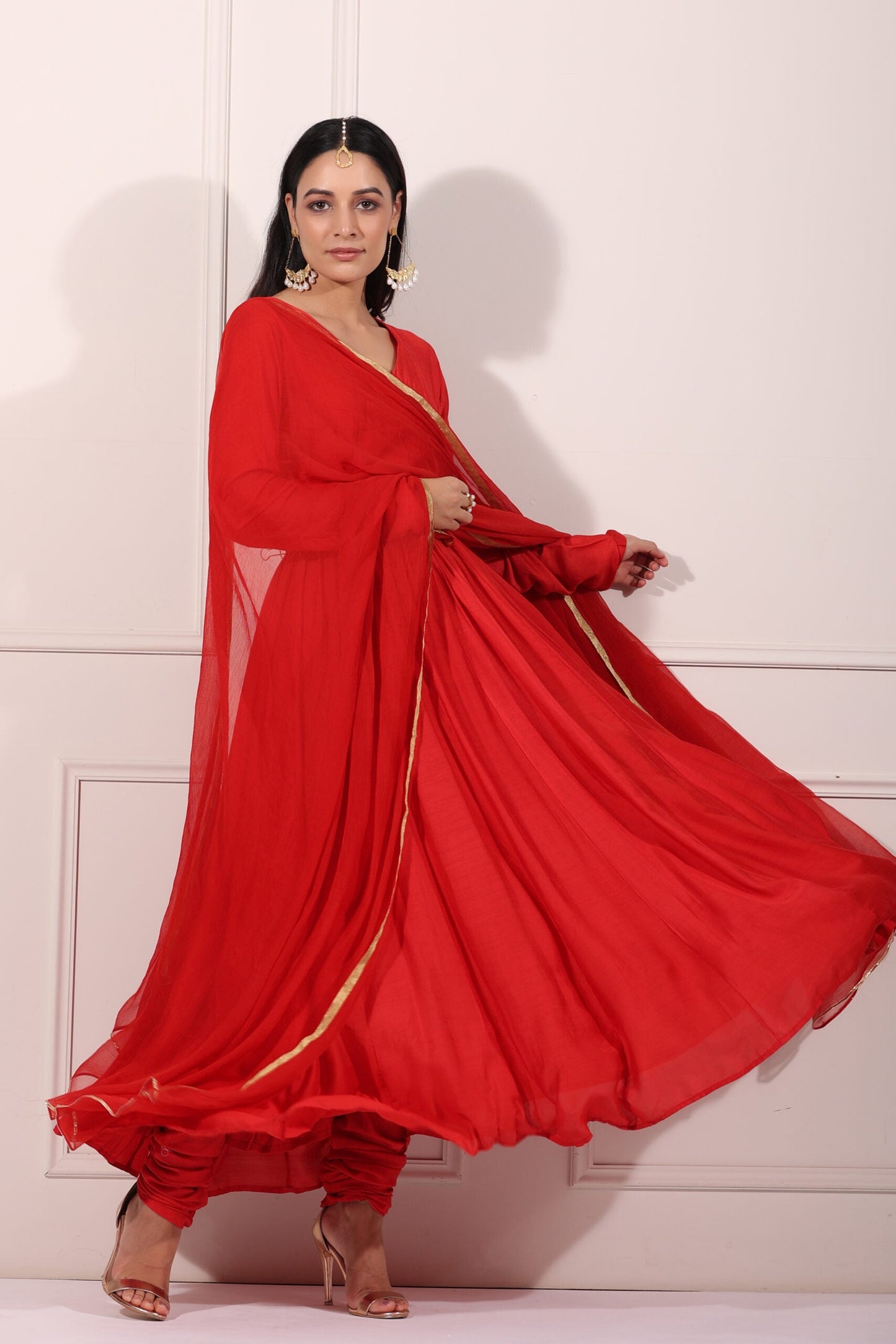Elegant red festive Anarkali gown flowing gracefully with a stylish silhouette and golden accents