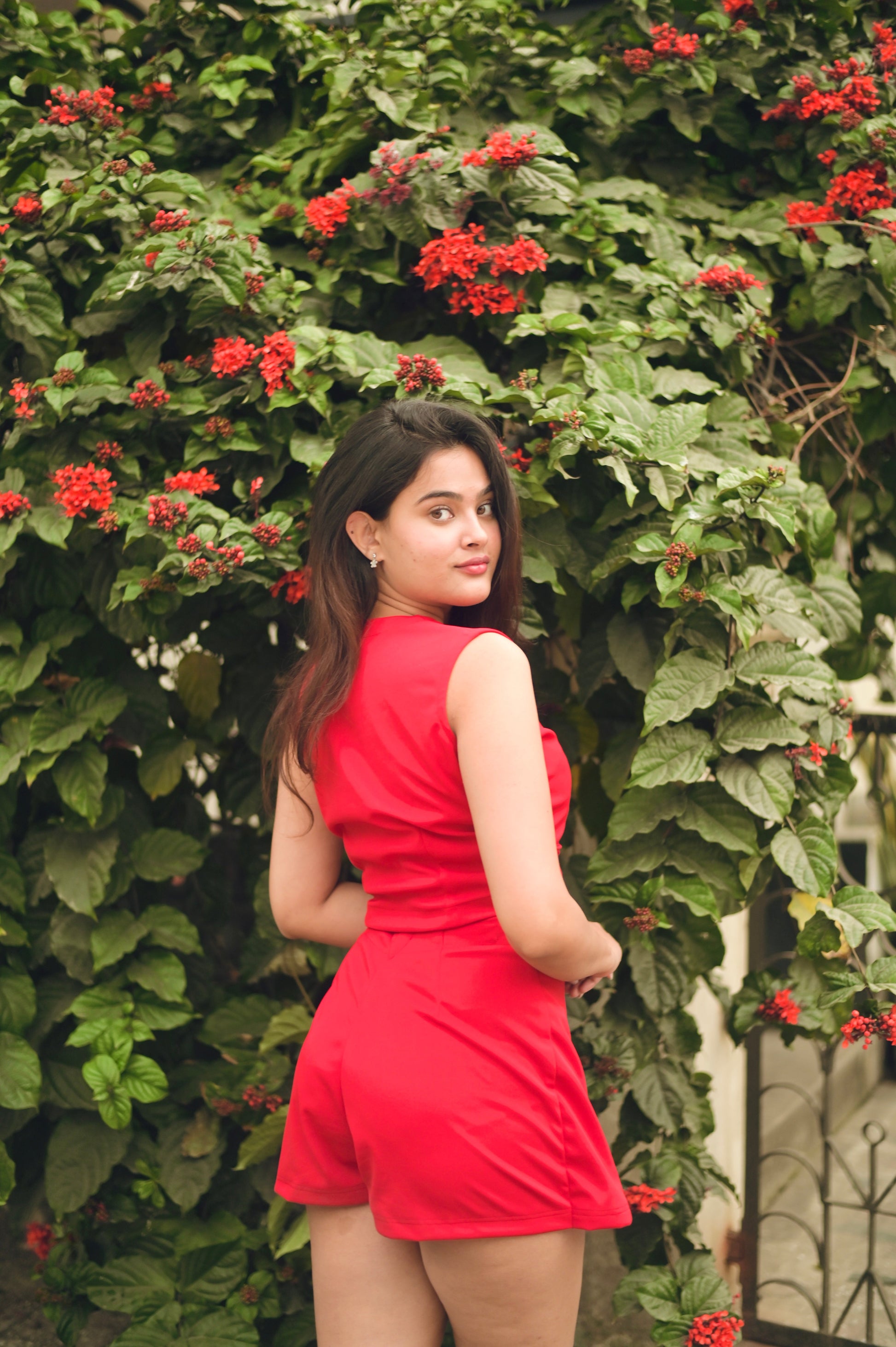 Model wearing red two piece set for women sleeveless crop top and high waisted shorts outdoors by flowering hedge