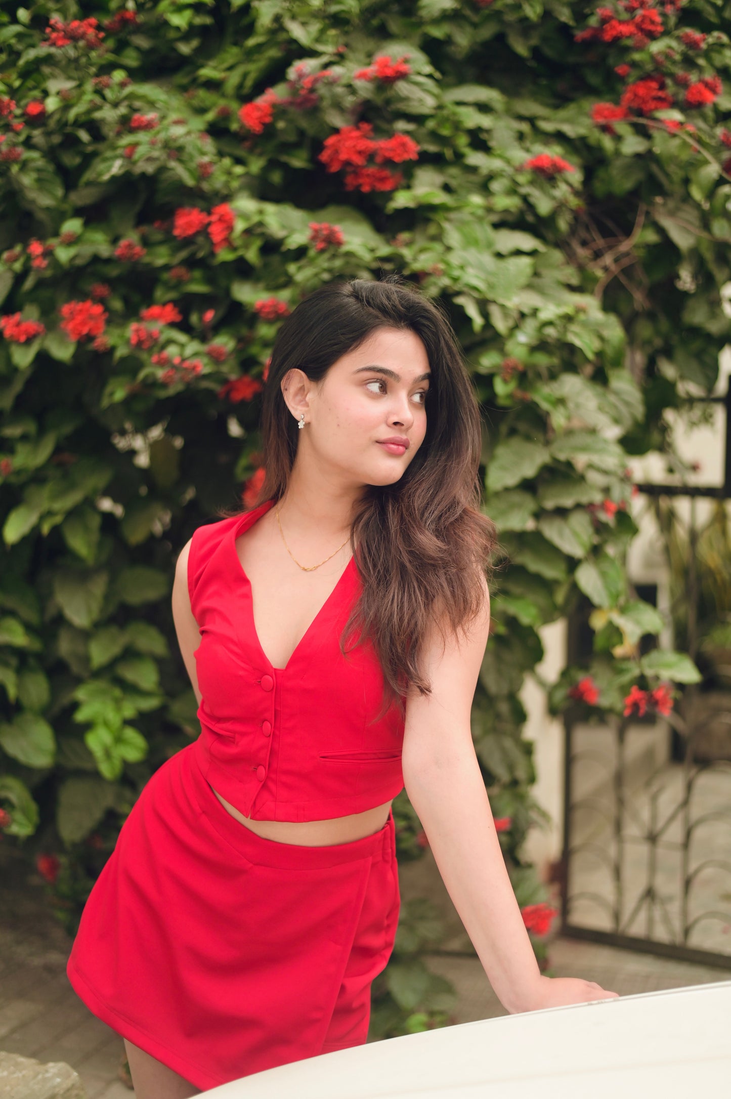 Model wearing a red two piece set for women with sleeveless V neck crop top and matching mini skirt in garden
