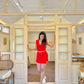 Stylera model wearing red two piece set for women standing in a bright cottage doorway