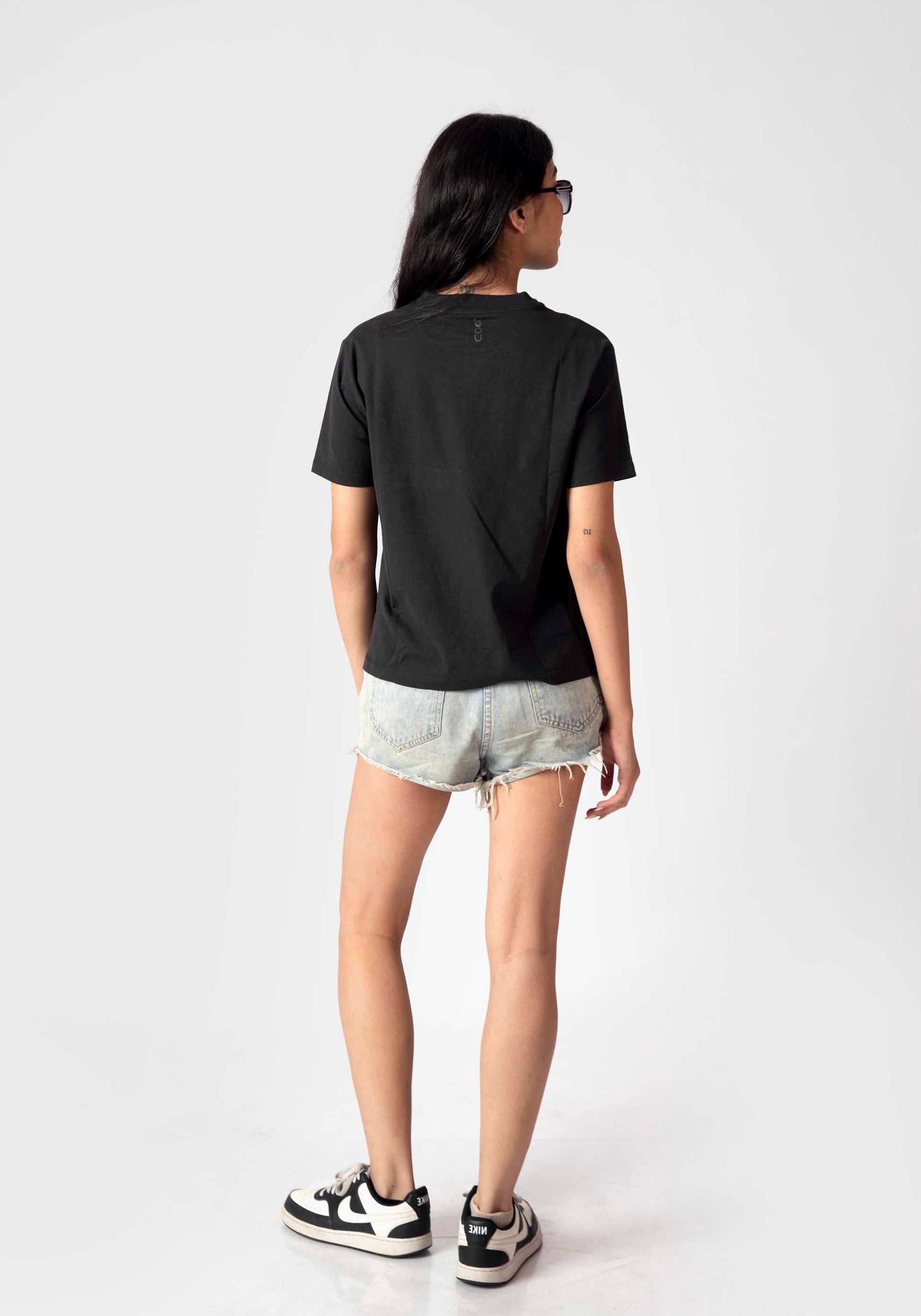 Woman wearing a regular fit black t-shirt for women by Stylera paired with denim shorts and sneakers