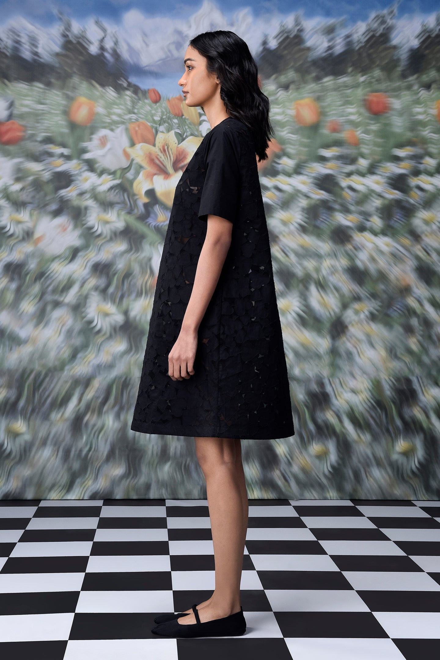 Side profile model wearing a relaxed fit black dress for women with short sleeves textured A line silhouette and black flats
