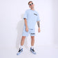 Stylera model wearing retro blue oversized t-shirt and matching shorts with white sneakers and sunglasses