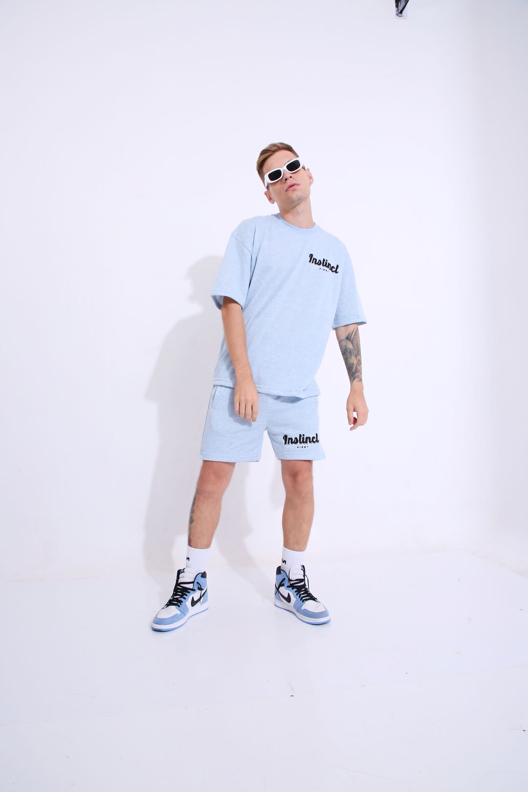 Stylera model wearing retro blue oversized t-shirt and matching shorts with white sneakers and sunglasses