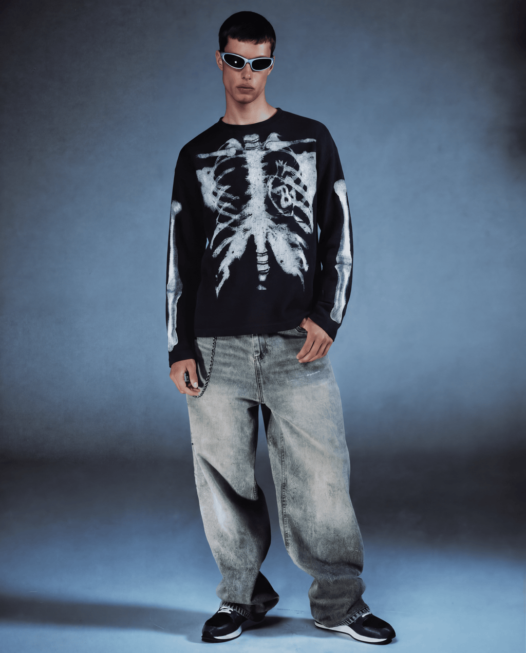Person wearing a black sweater with a white skeleton design and light blue jeans against a gray background