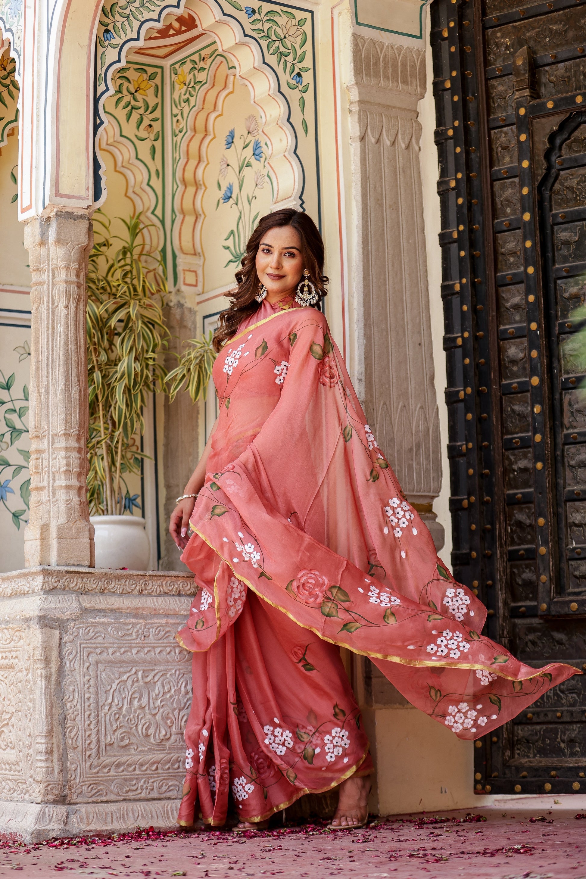 Elegant rust saree with floral hand painting showcased by a model in a beautiful setting
