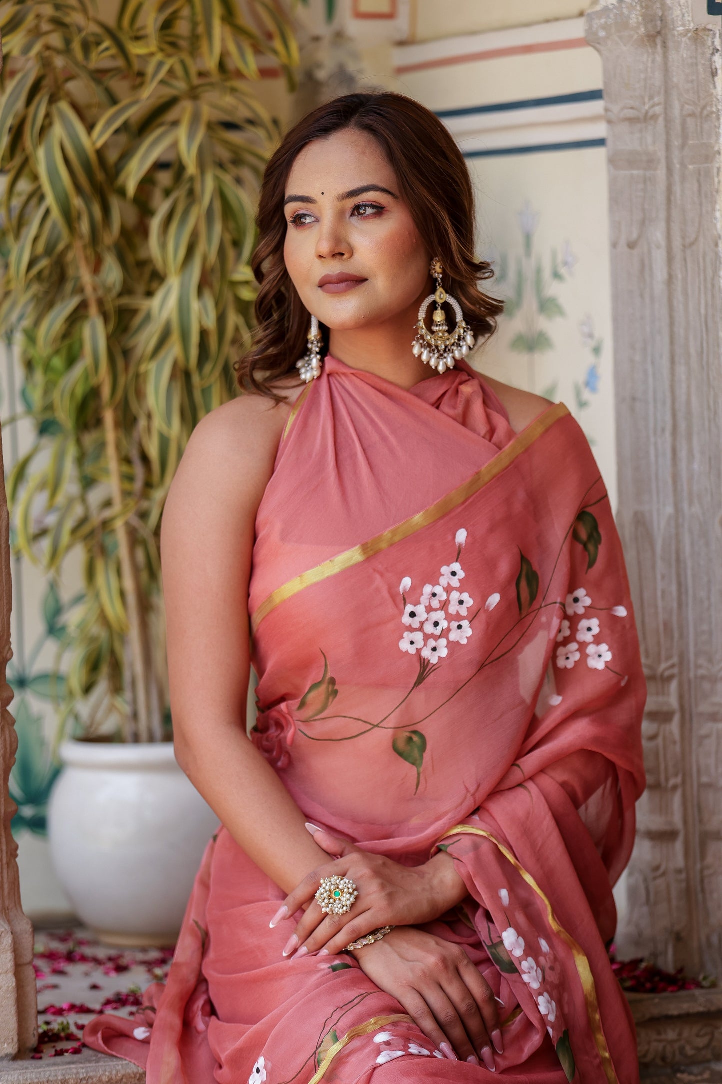 Elegant rust saree with floral hand painting, styled with statement earrings for a chic look