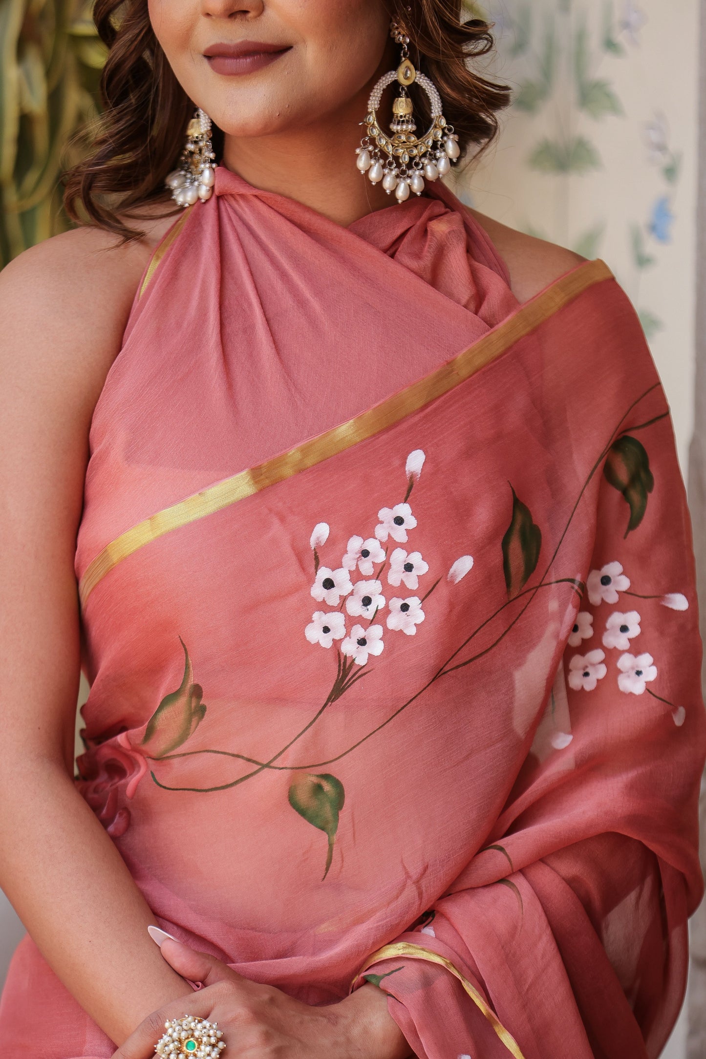 Elegant rust saree with floral hand painting and gold trim, styled for a sophisticated look