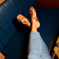 Trendy tan flats for women by Stylera worn with light blue jeans sitting on a dark blue bench