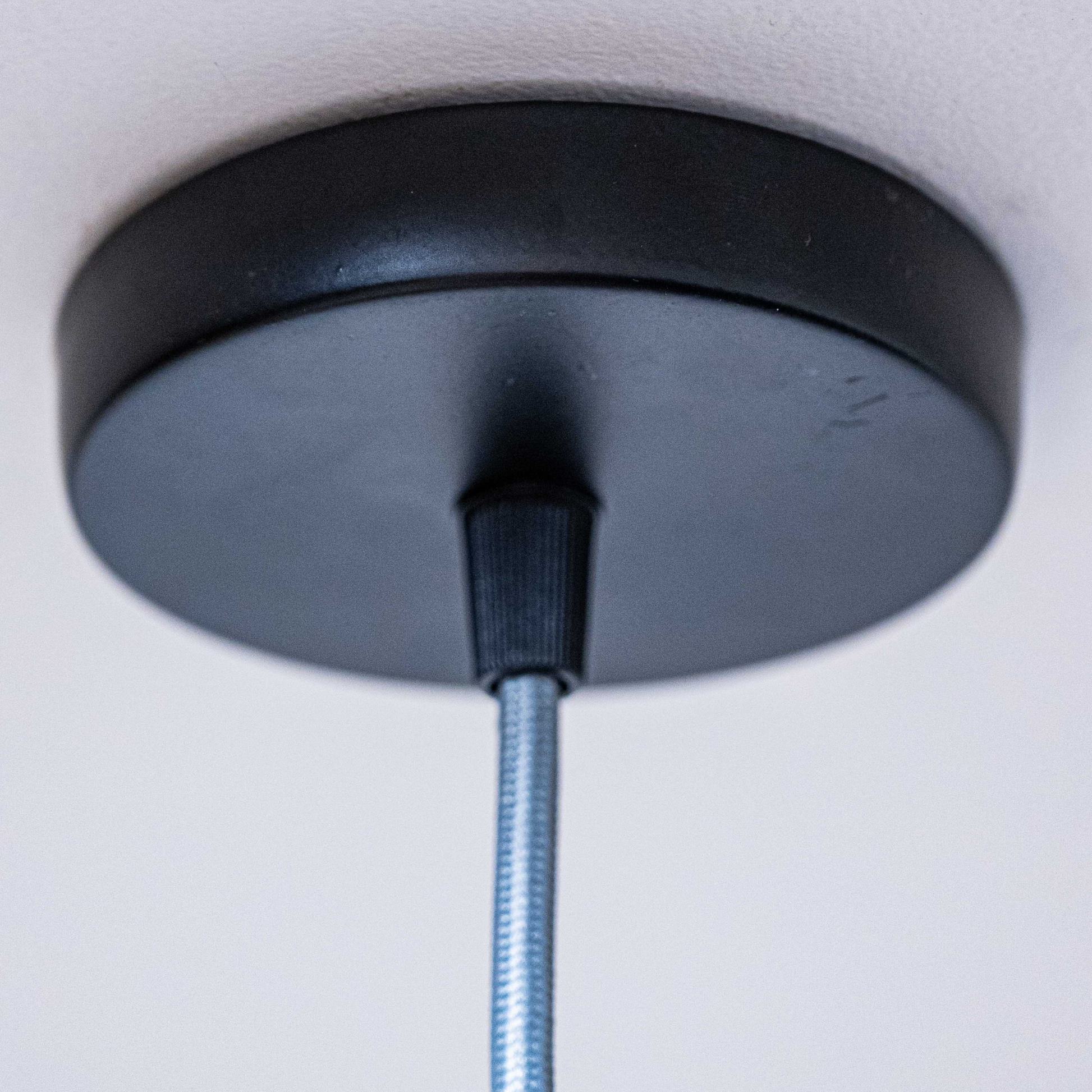 Black ceiling mount for sculpted white hanging lamp with sleek design and cord support