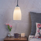 Sculpted white hanging lamp illuminating a cozy bedroom with a bedside table and decorative items