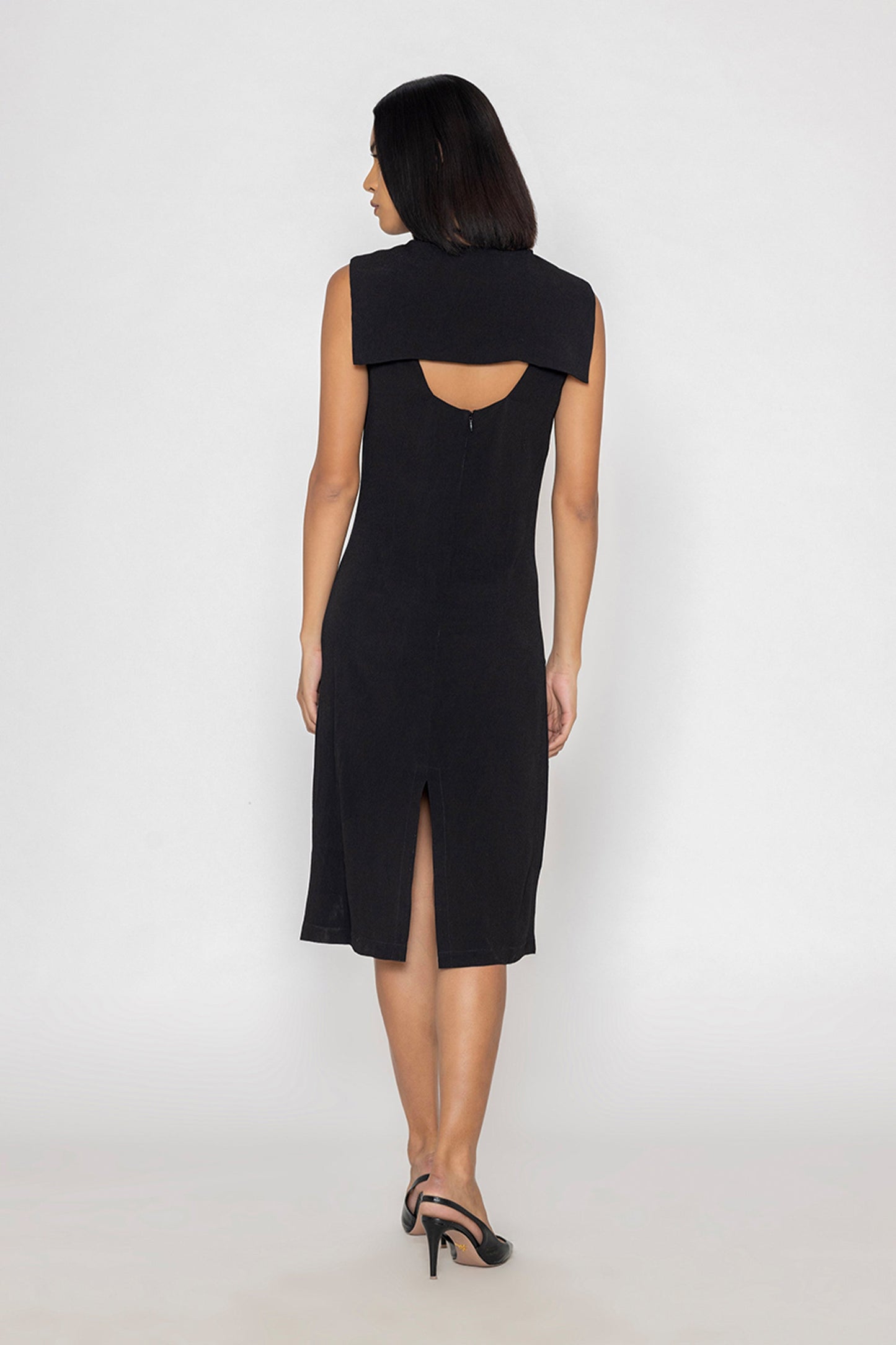 Back view of a model wearing Stylera sleek black evening dress with sleeveless design and back slit