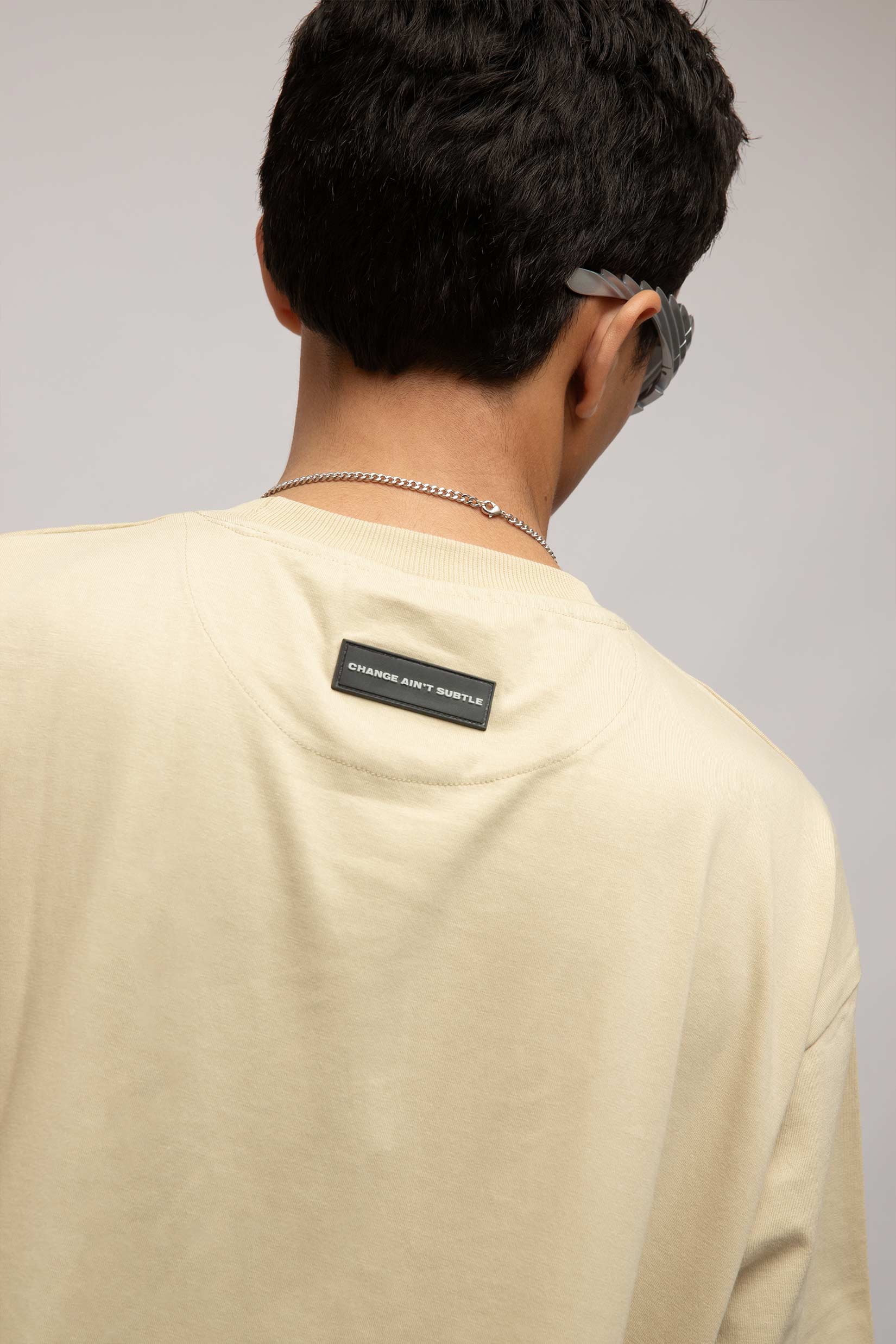 Back view of model wearing Stylera cream crewneck with branded neck label stencil art t-shirt relaxed fit