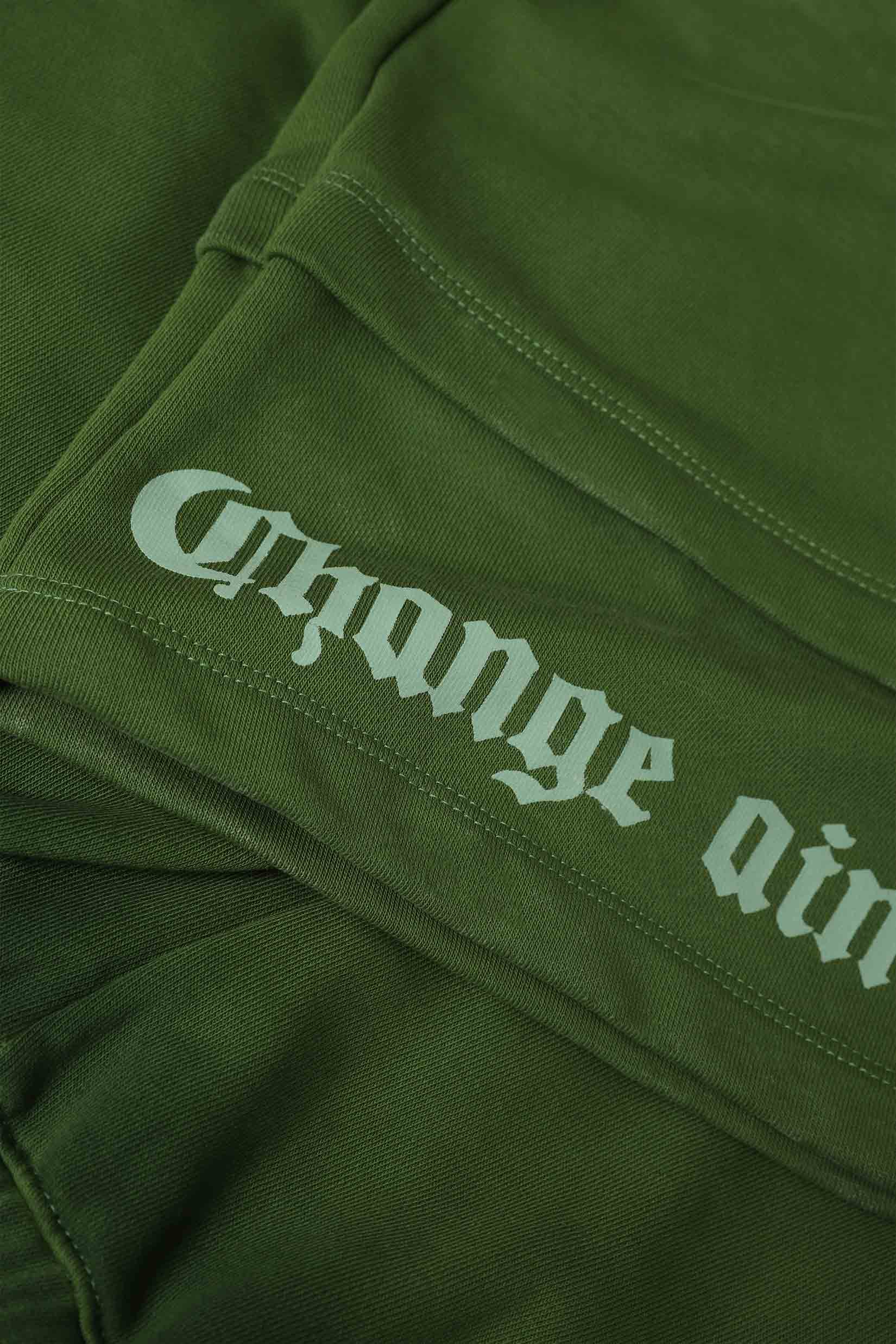 Stylera olive green cargo pocket joggers closeup showing folded fabric seam and white gothic text print on leg