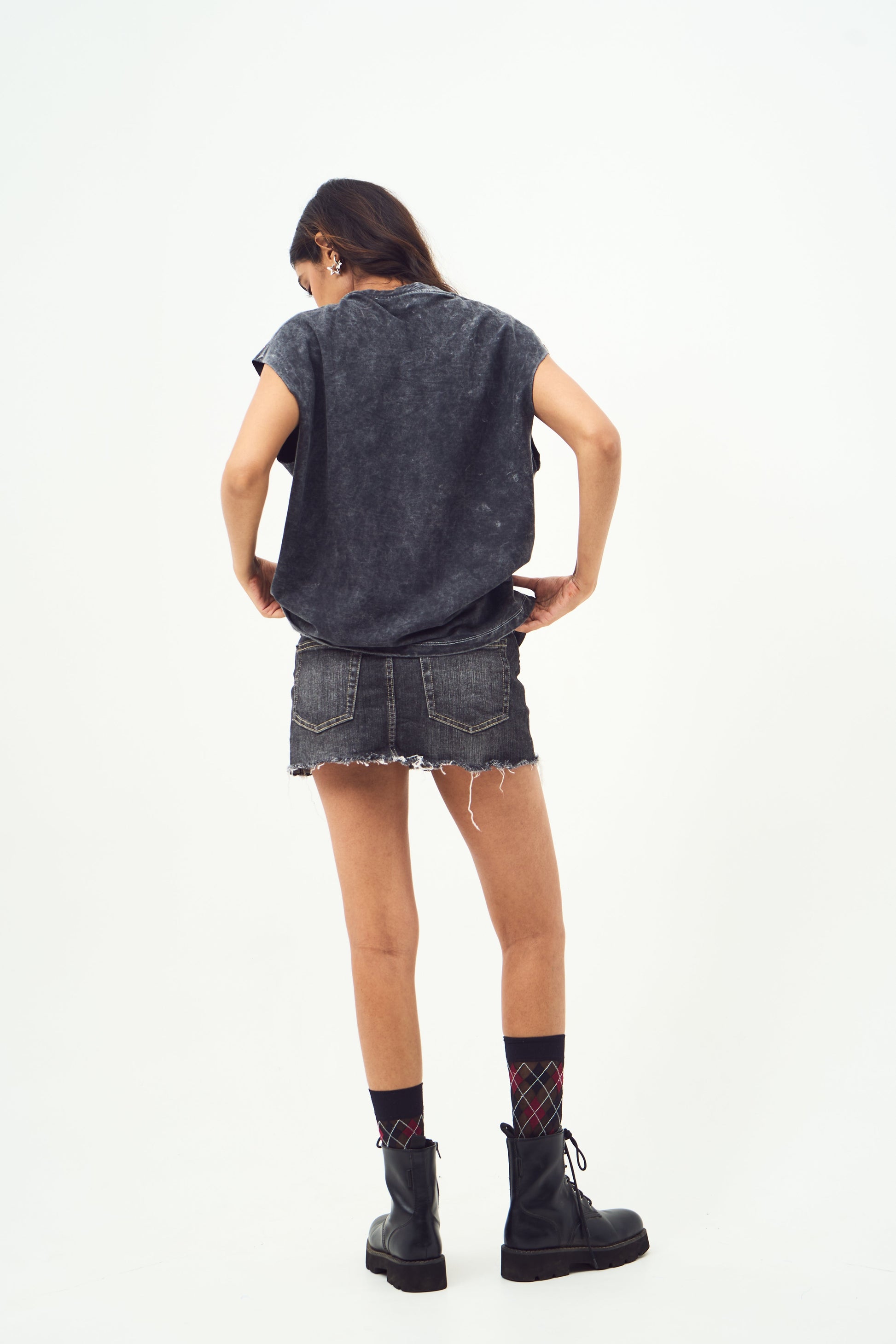 Back view of model wearing Stylera red graphic sleeveless t-shirt styled with frayed denim skirt and boots