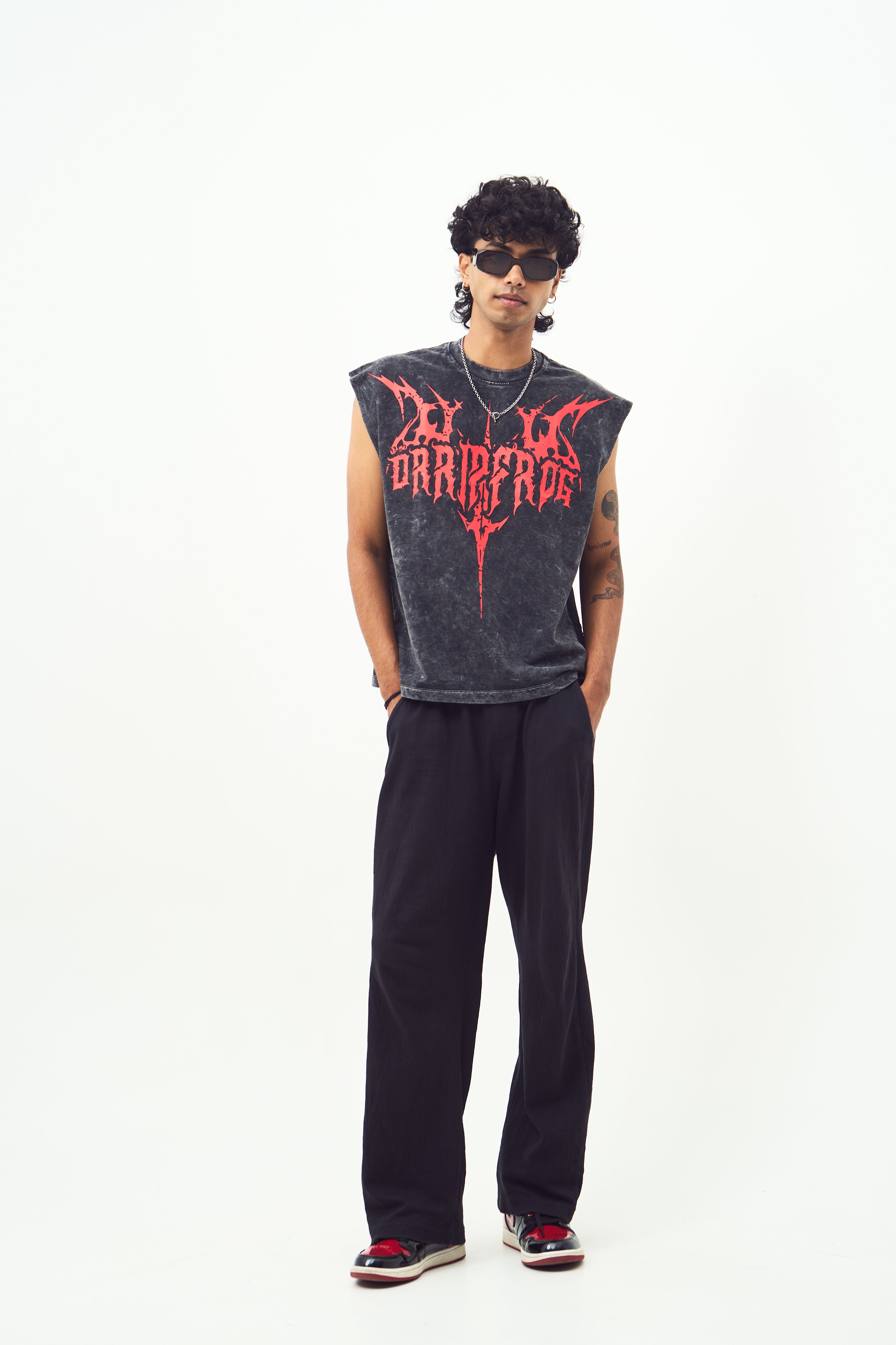 Male model wearing Stylera red graphic sleeveless t-shirt with extended shoulders black wide pants and sunglasses