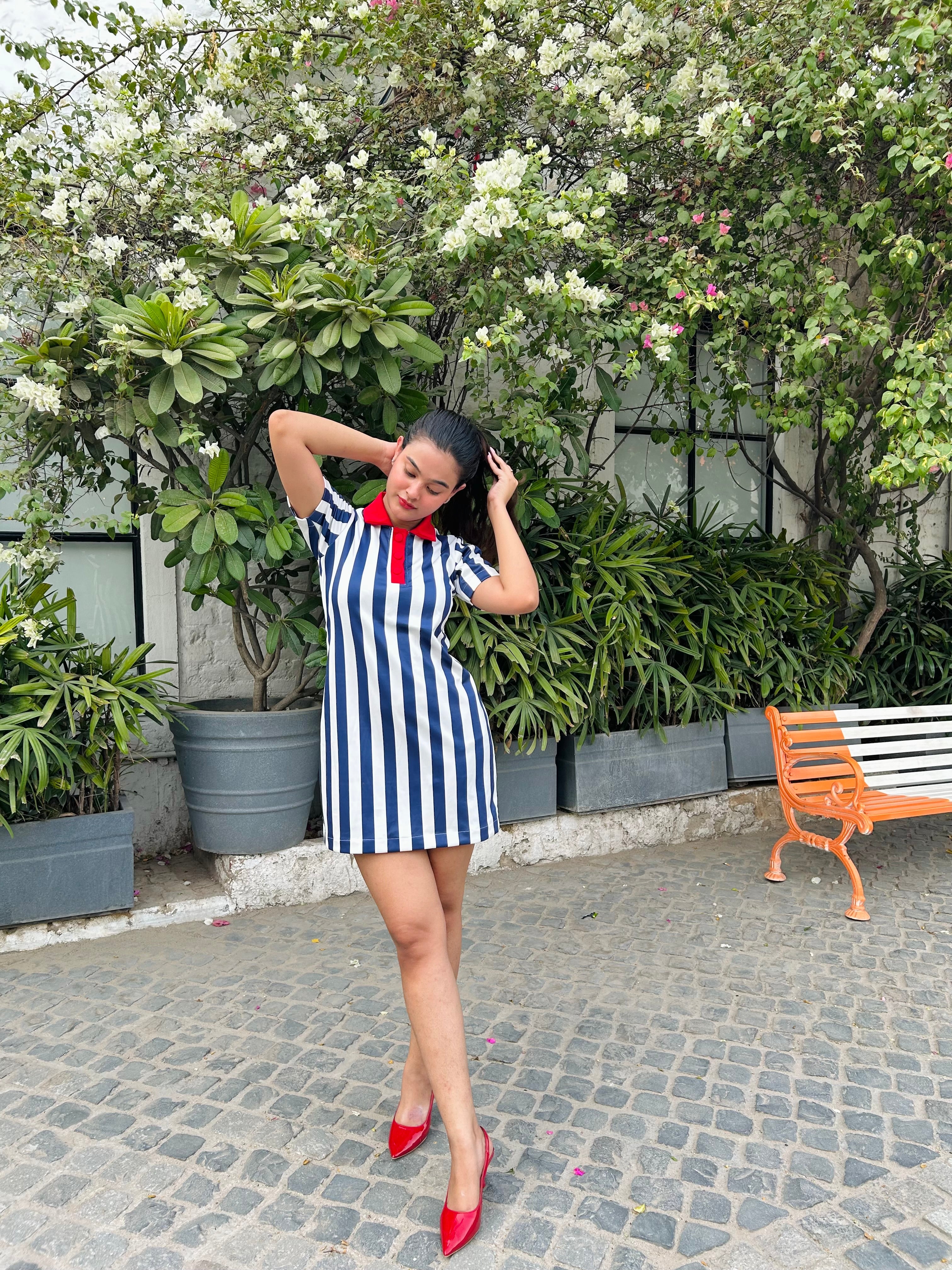 Model posing outdoors in a navy and white striped mini dress for women with red collar tie and red heels
