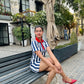 Young woman seated on a bench in a courtyard wearing striped mini dress for women with red collar and red heels