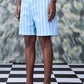 Stylera striped regular fit shorts in pastel blue and white vertical stripes on model with black sandals