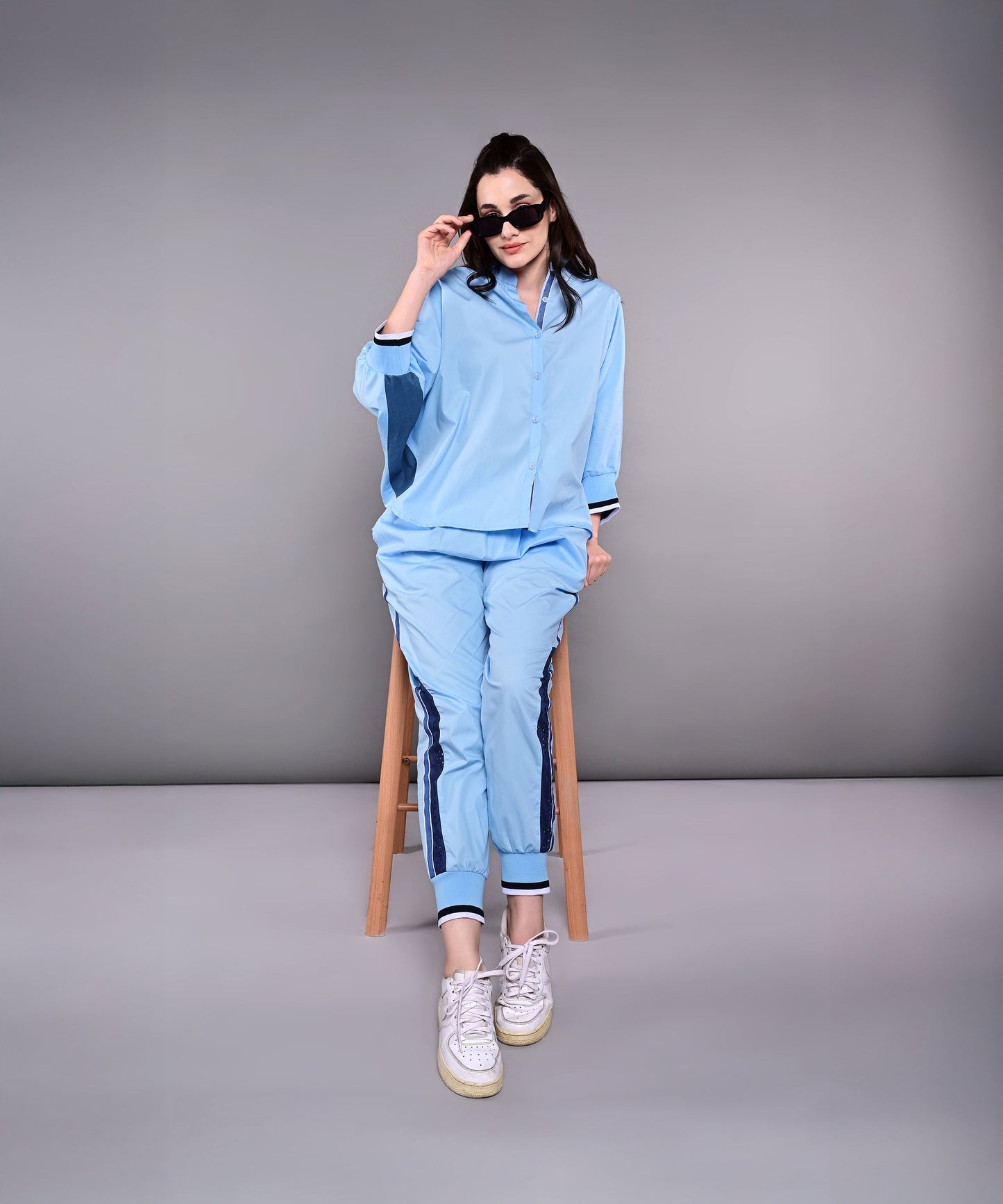 Woman wearing a stylish denim track suit in blue, paired with sunglasses and sneakers for a chic look