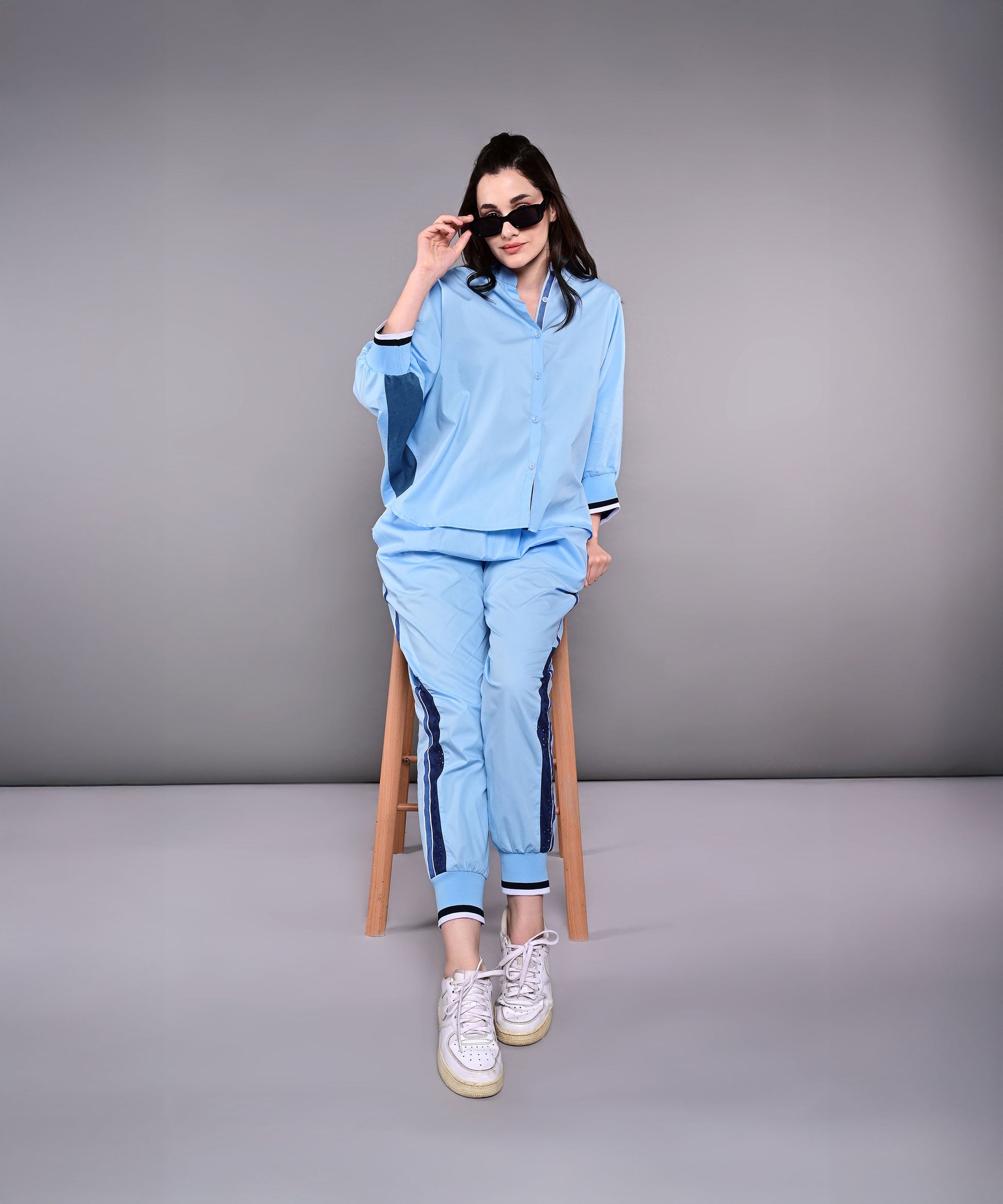 Woman wearing a stylish denim track suit in blue, paired with sunglasses and sneakers for a chic look