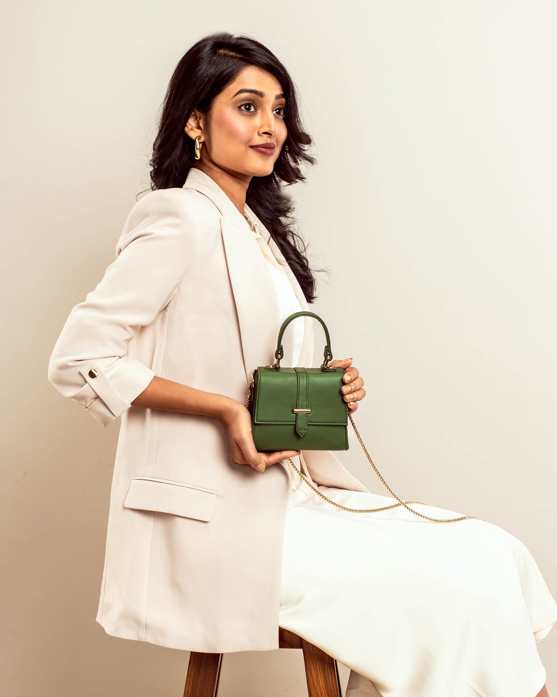 Stylish green purse with gold chain held by a woman in a white blazer for a chic look