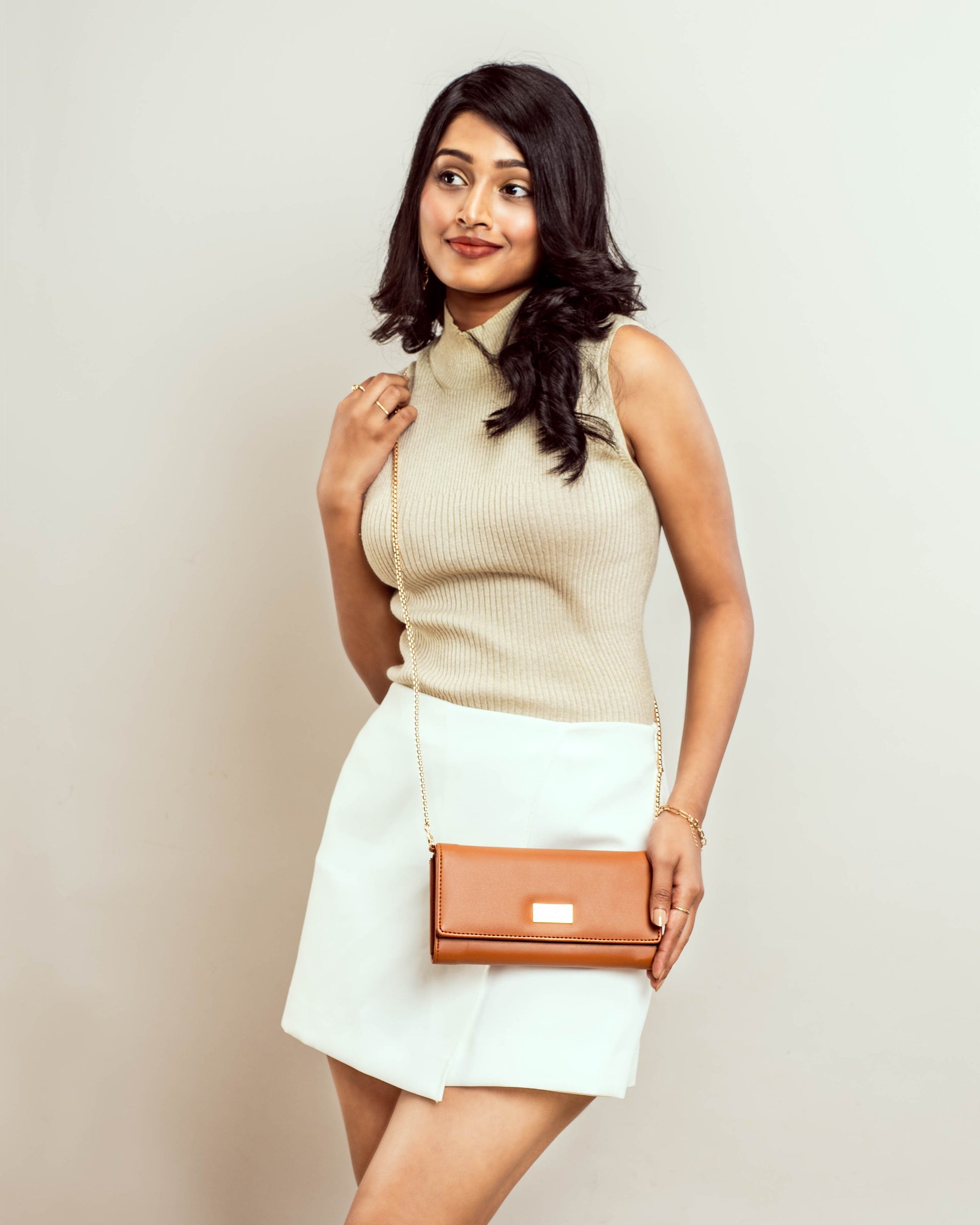 Stylish tan evening bag styled with a beige top and white skirt for a chic look
