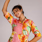 Model wearing a summer pink cotton dress with vibrant floral patterns, holding an orange fruit