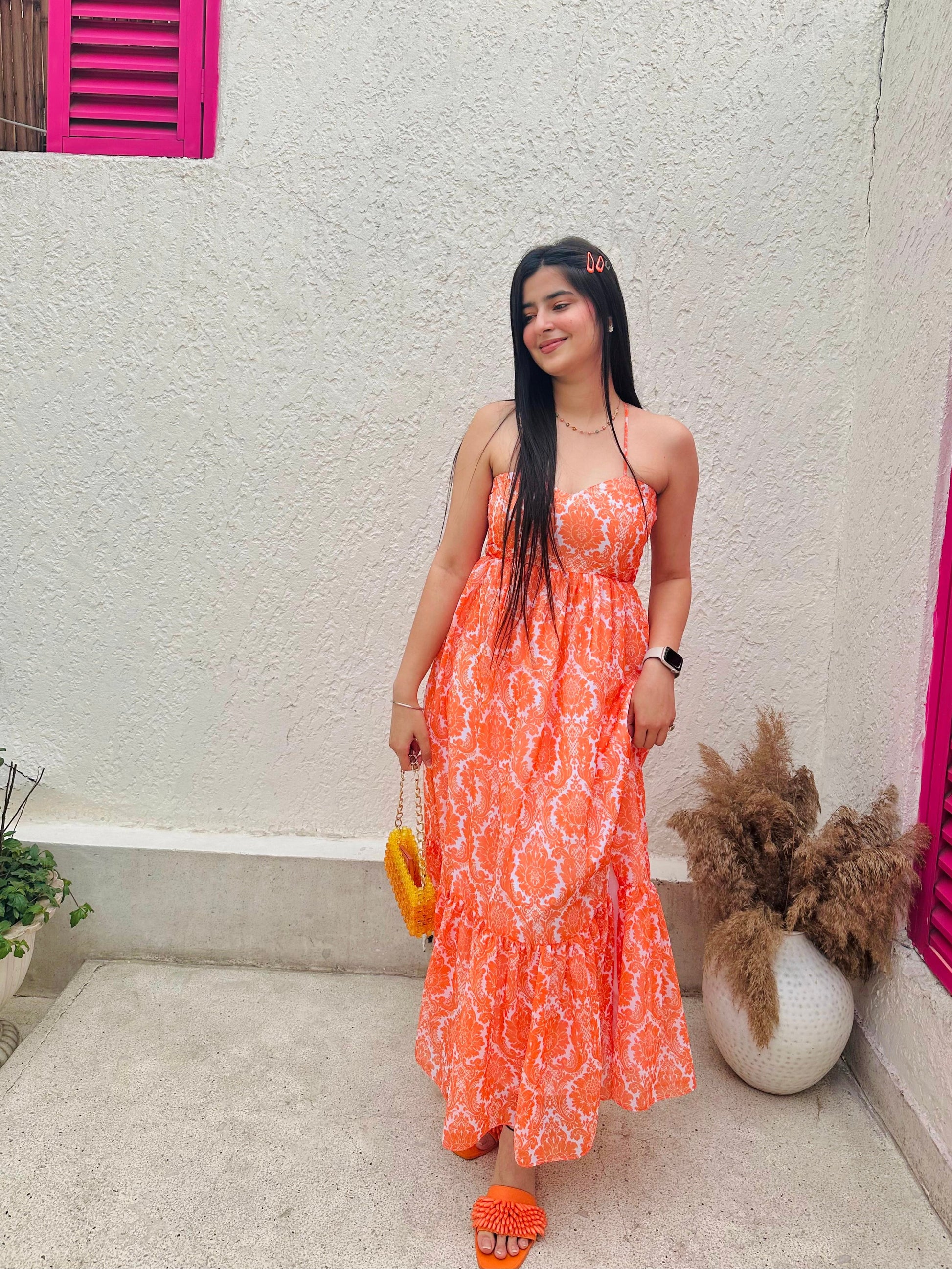 Woman in orange patterned casual backless maxi dress with yellow woven bag and matching sandals in courtyard