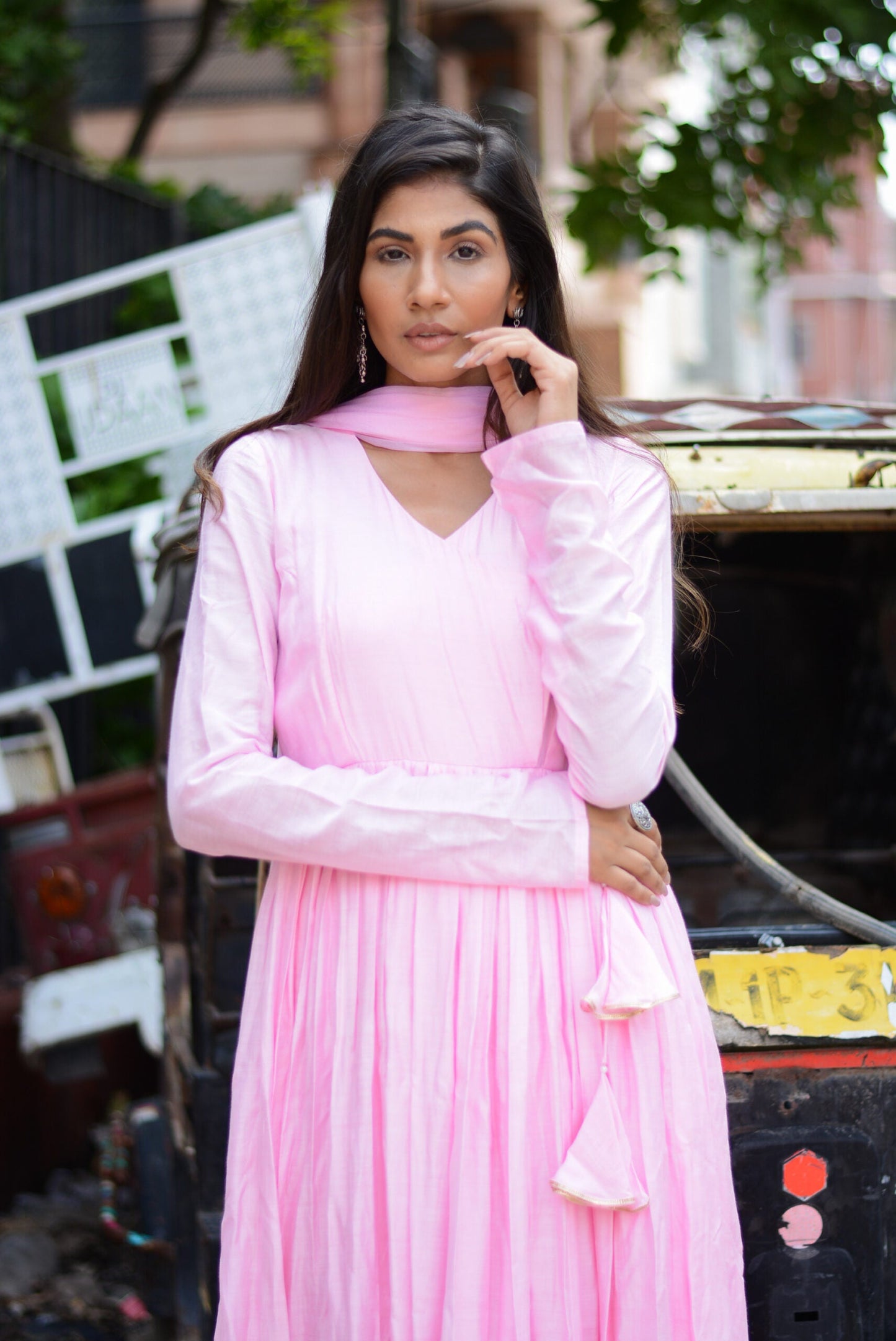 Model wearing a taffy pink anarkali suit set with elegant pleats and matching dupatta in a street setting