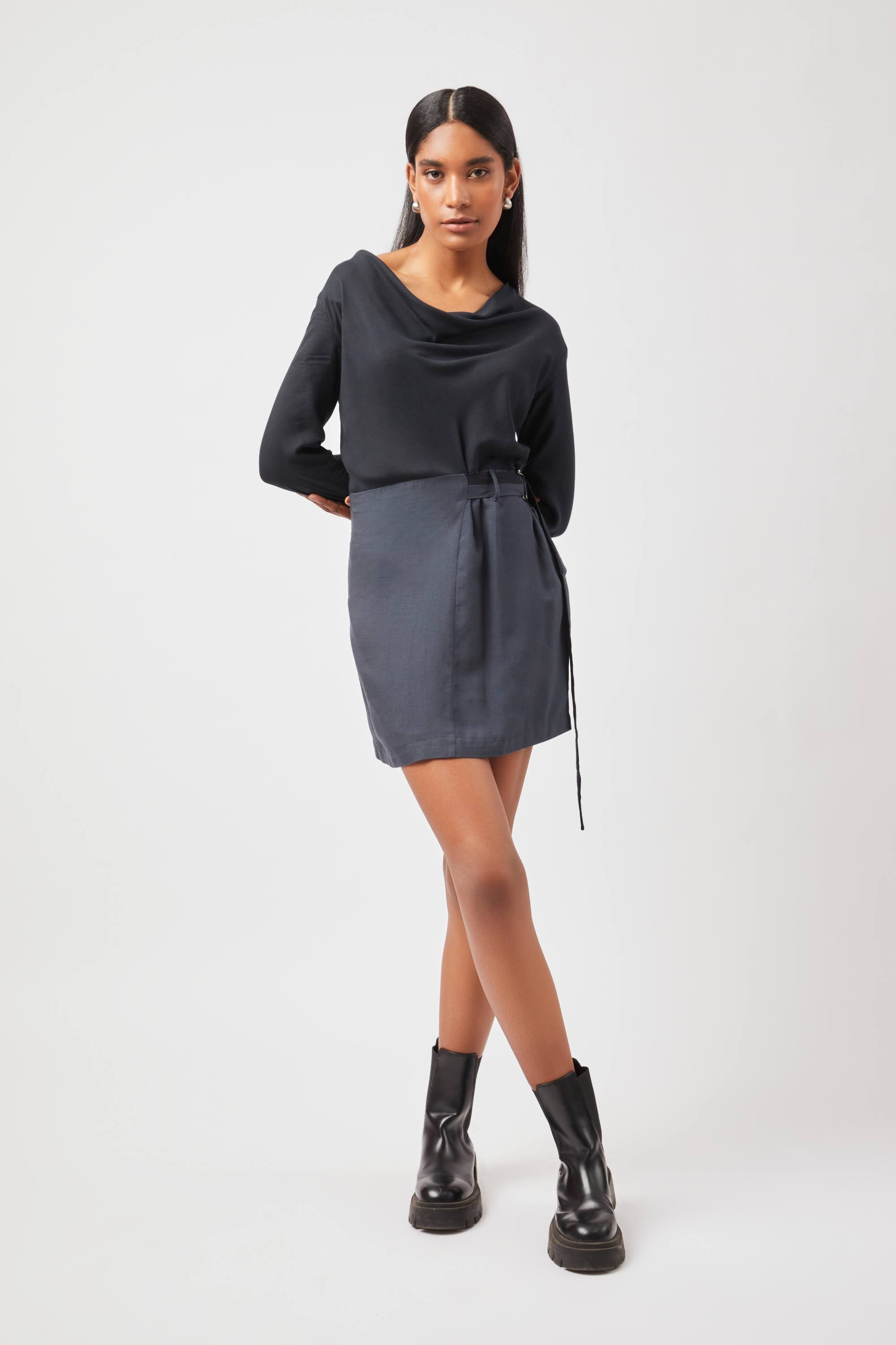 Stylera Tate cowl neck dress in black with long sleeves and a waist tie worn with black ankle boots