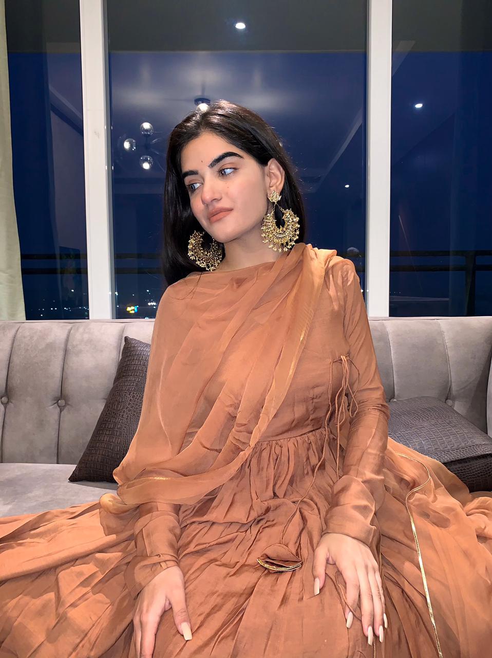 Elegant traditional Anarkali gown caramel with intricate draping and stylish earrings for festive occasions