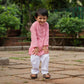 Smiling boy wearing a pink traditional kurta pajama for boys with white pants and sandals outdoors