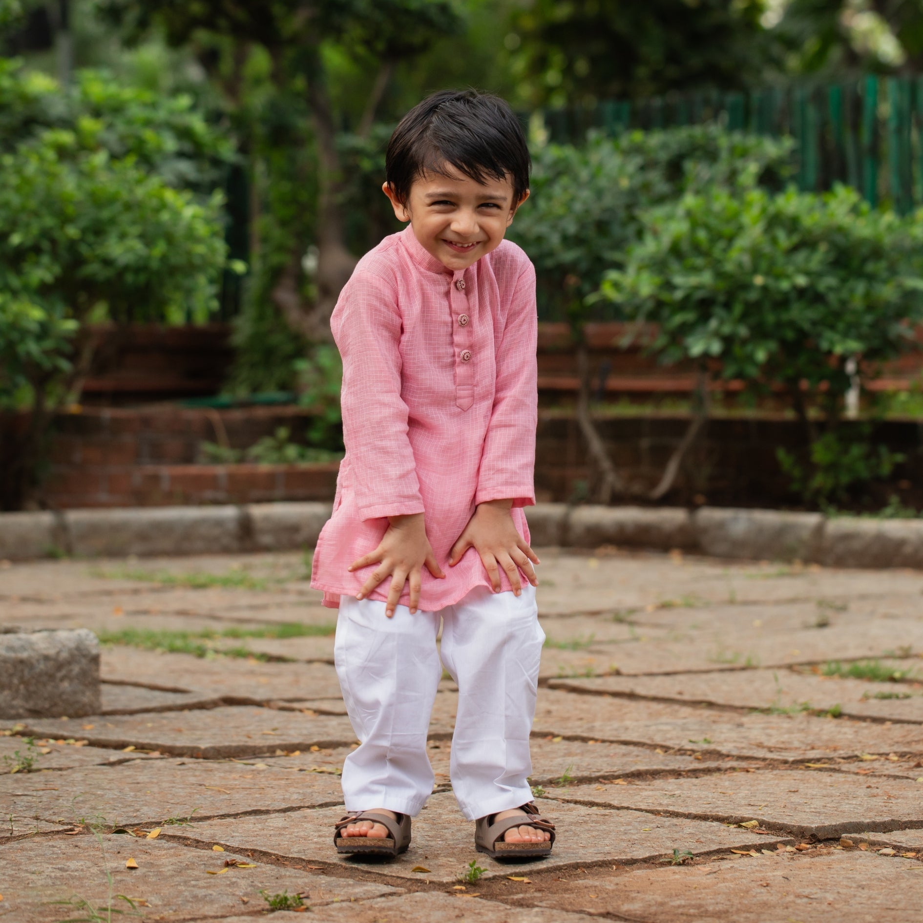 Smiling boy wearing a pink traditional kurta pajama for boys with white pants and sandals outdoors