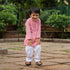 Smiling boy wearing a pink traditional kurta pajama for boys with white pants and sandals outdoors