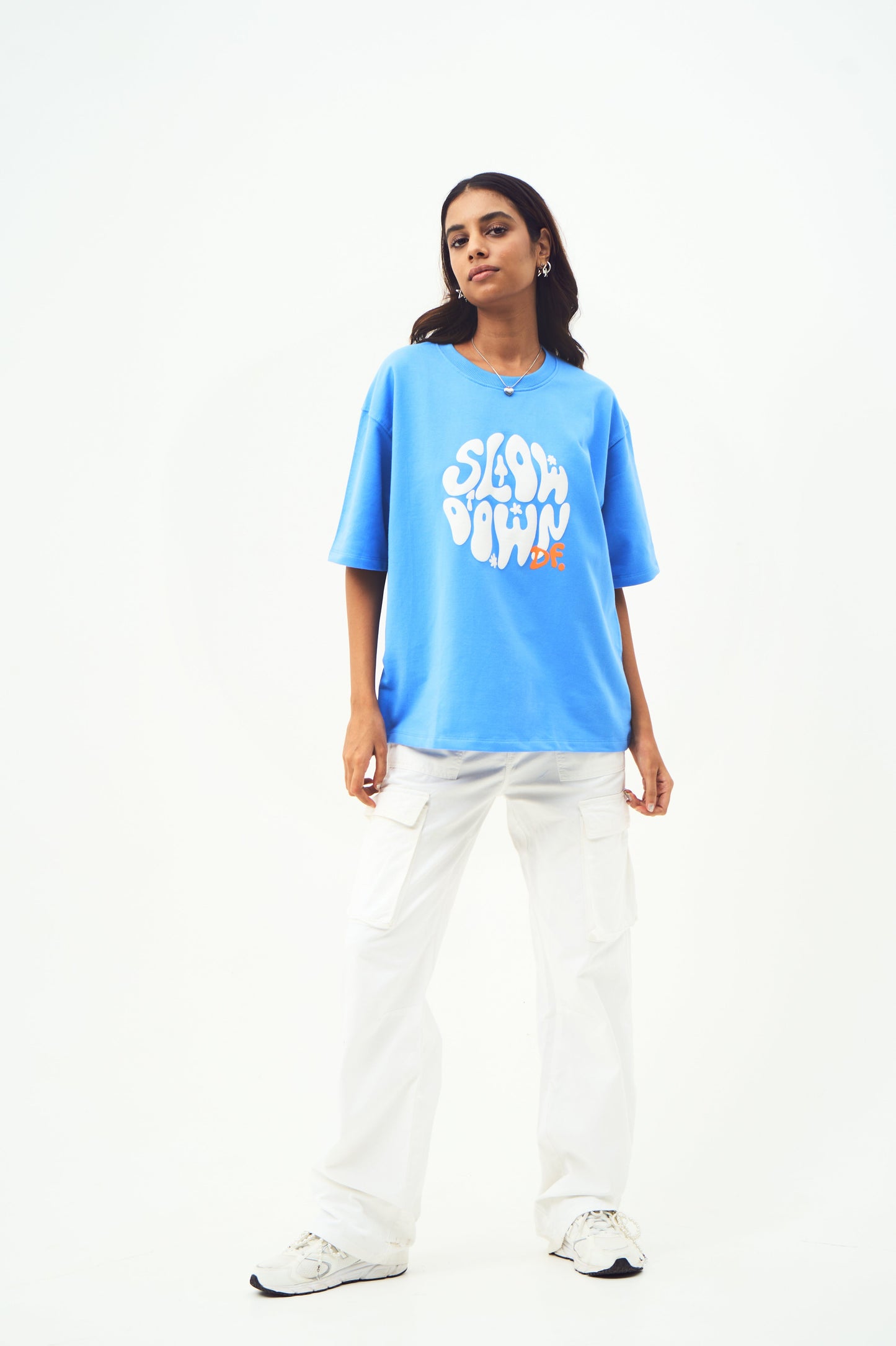 Model wearing Stylera trendy blue t-shirt for men and women oversized fit white graphic with white pants and sneakers