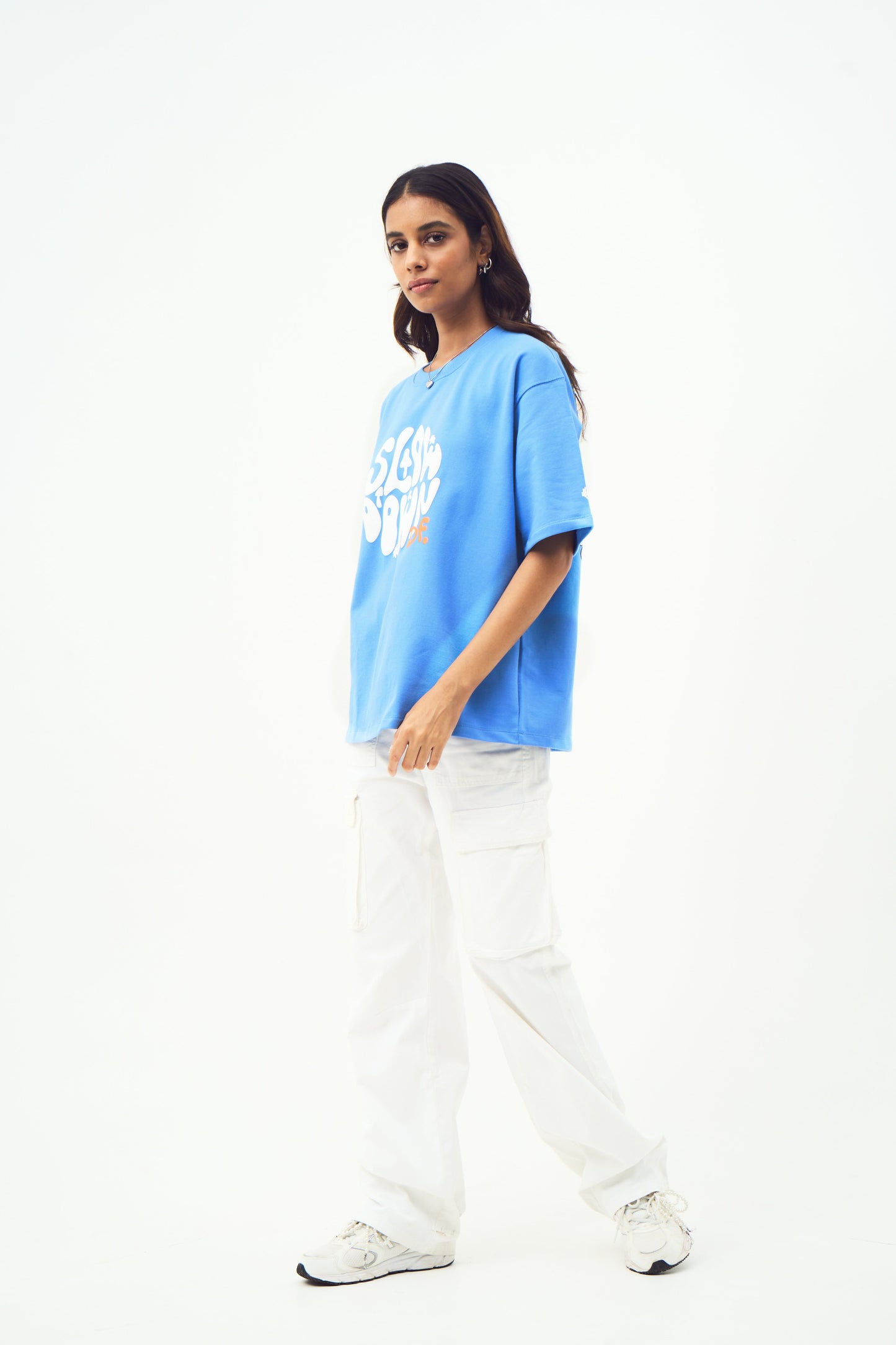 Female model wearing Stylera trendy blue t-shirt for men and women oversized fit with white cargo pants
