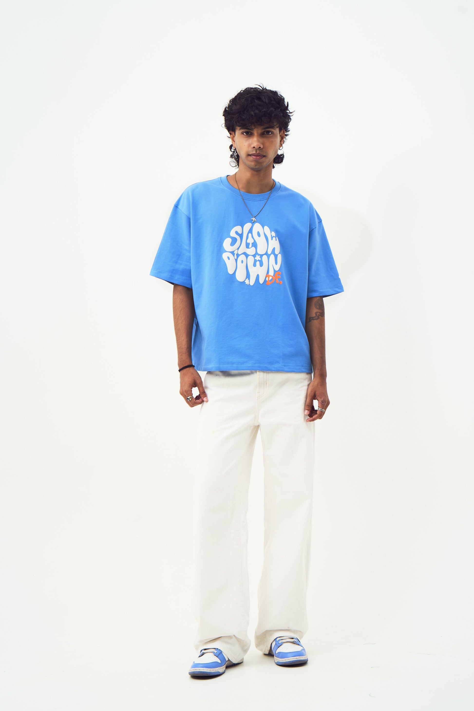 Male model wearing Stylera trendy blue t-shirt for men and women with white graphic print relaxed fit and white pants