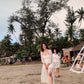 Model wearing a trendy evening maxi dress with a thigh-high slit, walking on a beach surrounded by palm trees