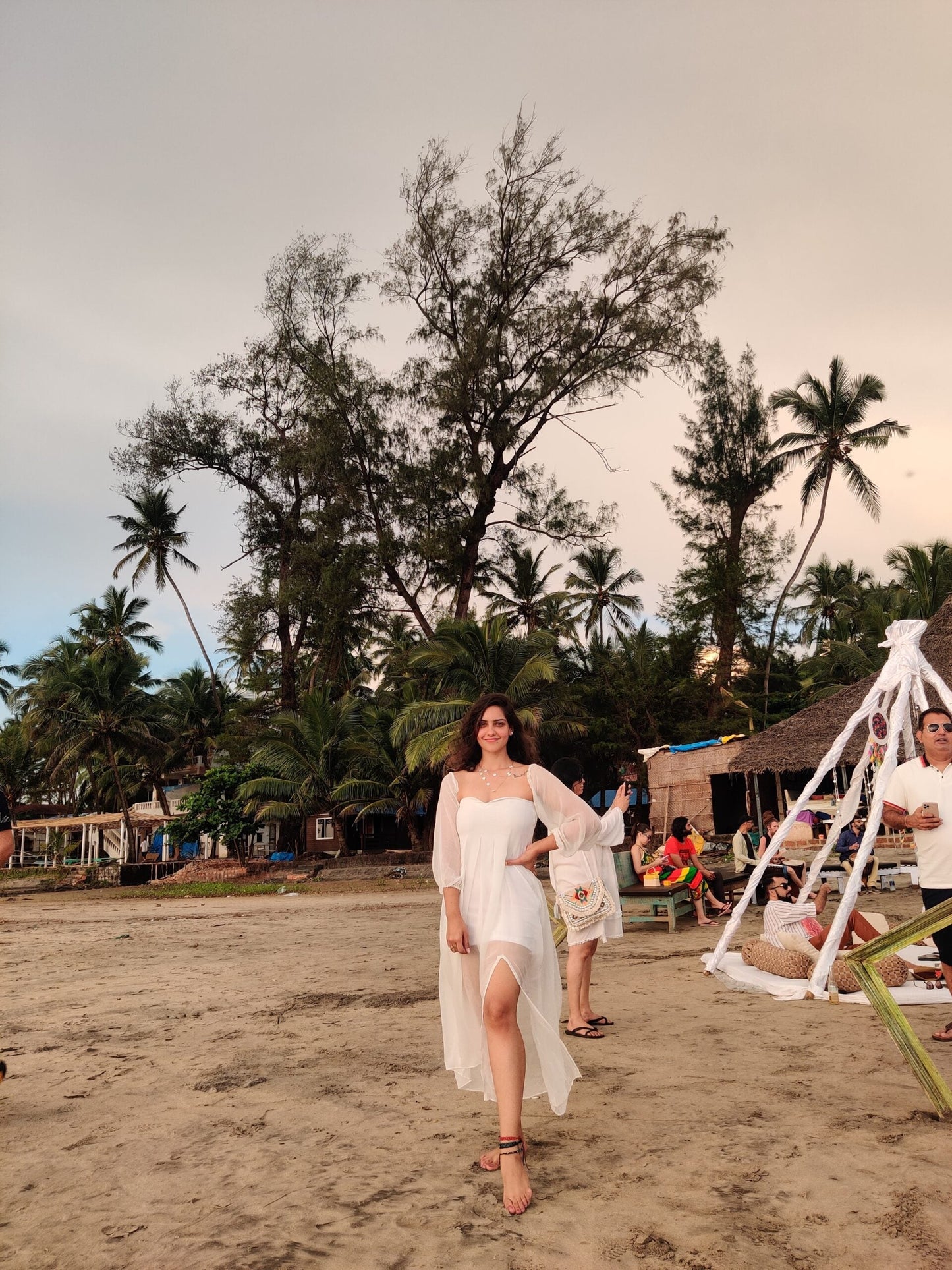 Model wearing a trendy evening maxi dress with a flowing design on the beach surrounded by palm trees