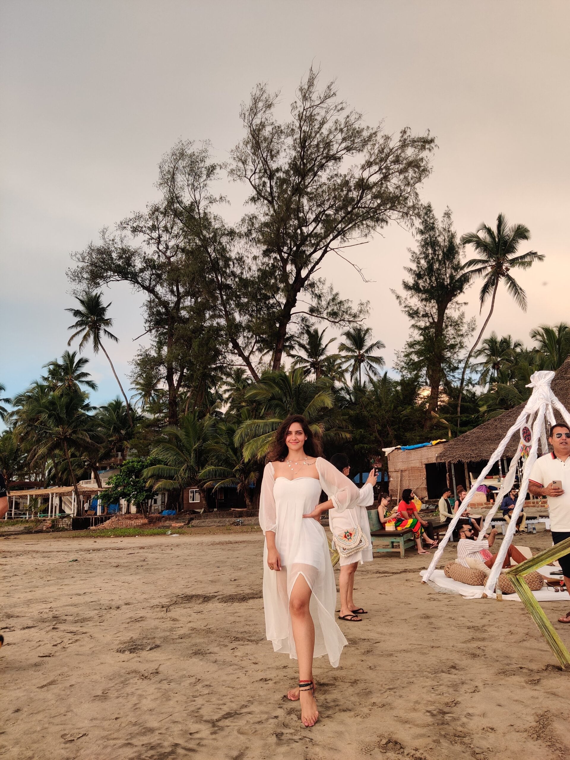Model wearing a trendy evening maxi dress with a flowing design on the beach surrounded by palm trees