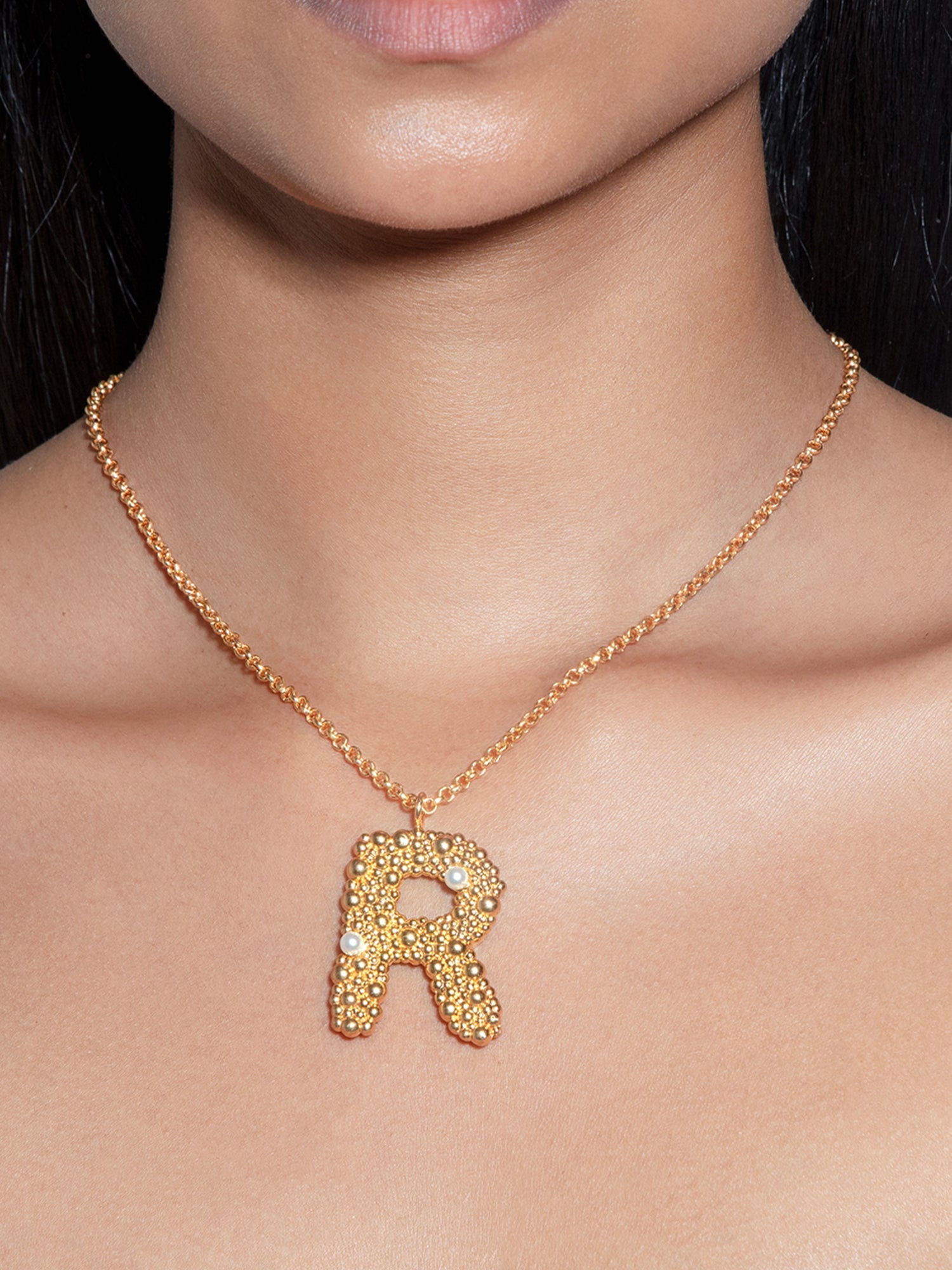 Stylera trendy gold R pendant necklace on model with textured beaded R and small pearl accents