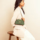 Stylish woman wearing a trendy green handbag with a chain strap, seated on a wooden stool