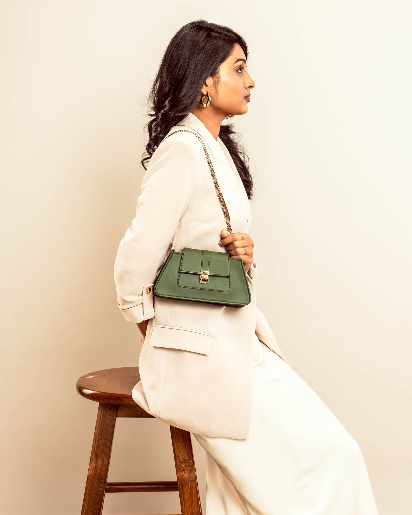 Stylish woman wearing a trendy green handbag with a chain strap, seated on a wooden stool