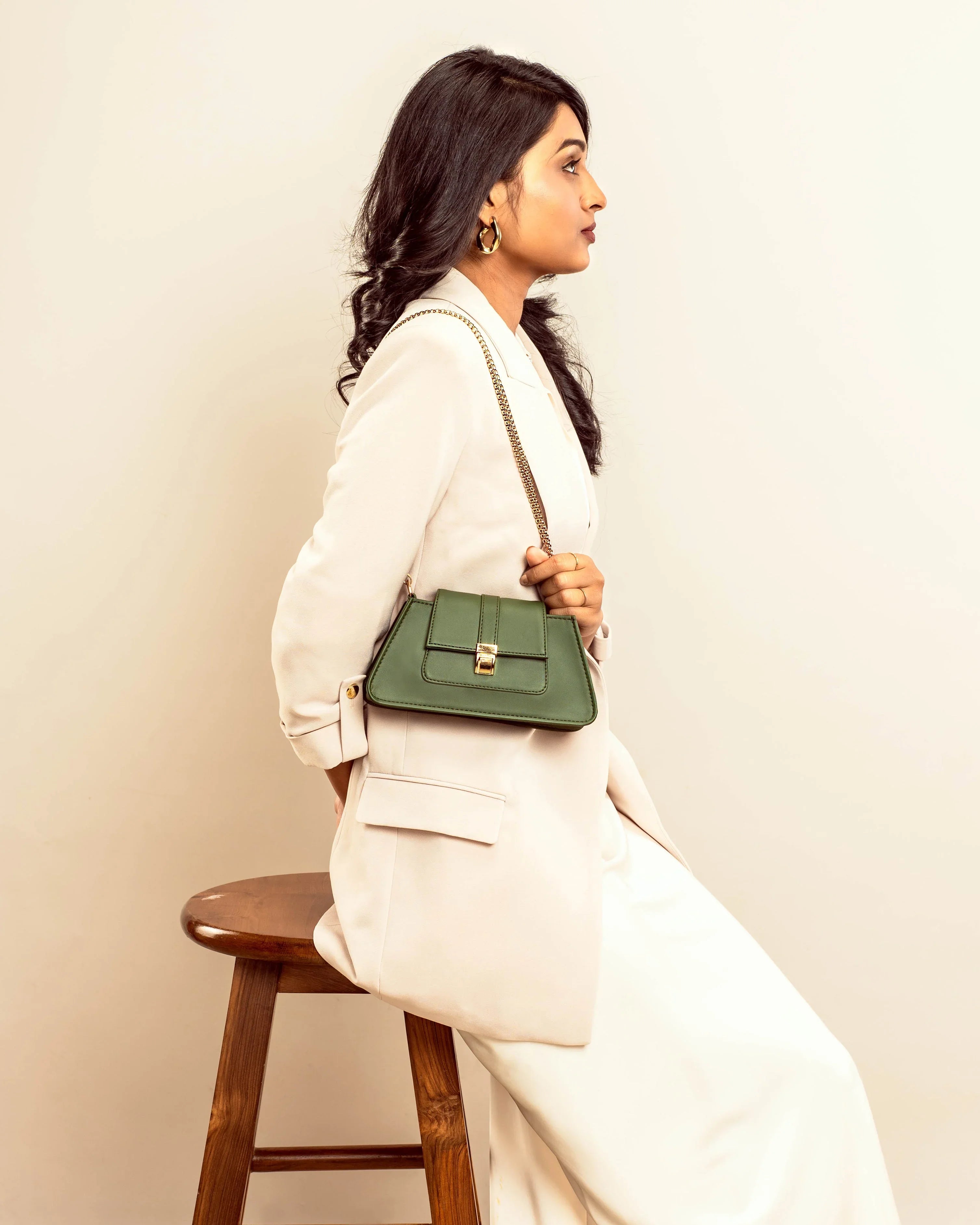 Stylish woman wearing a trendy green handbag with a chain strap, seated on a wooden stool