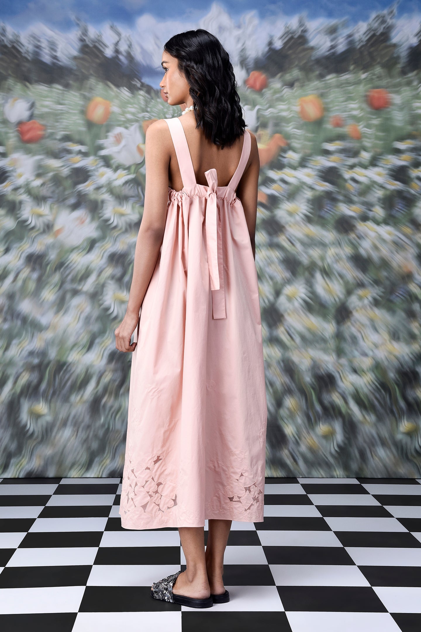 Back view of woman wearing pink bow tie back dress with cutwork hem trendy maxi dress for women on checkered floor
