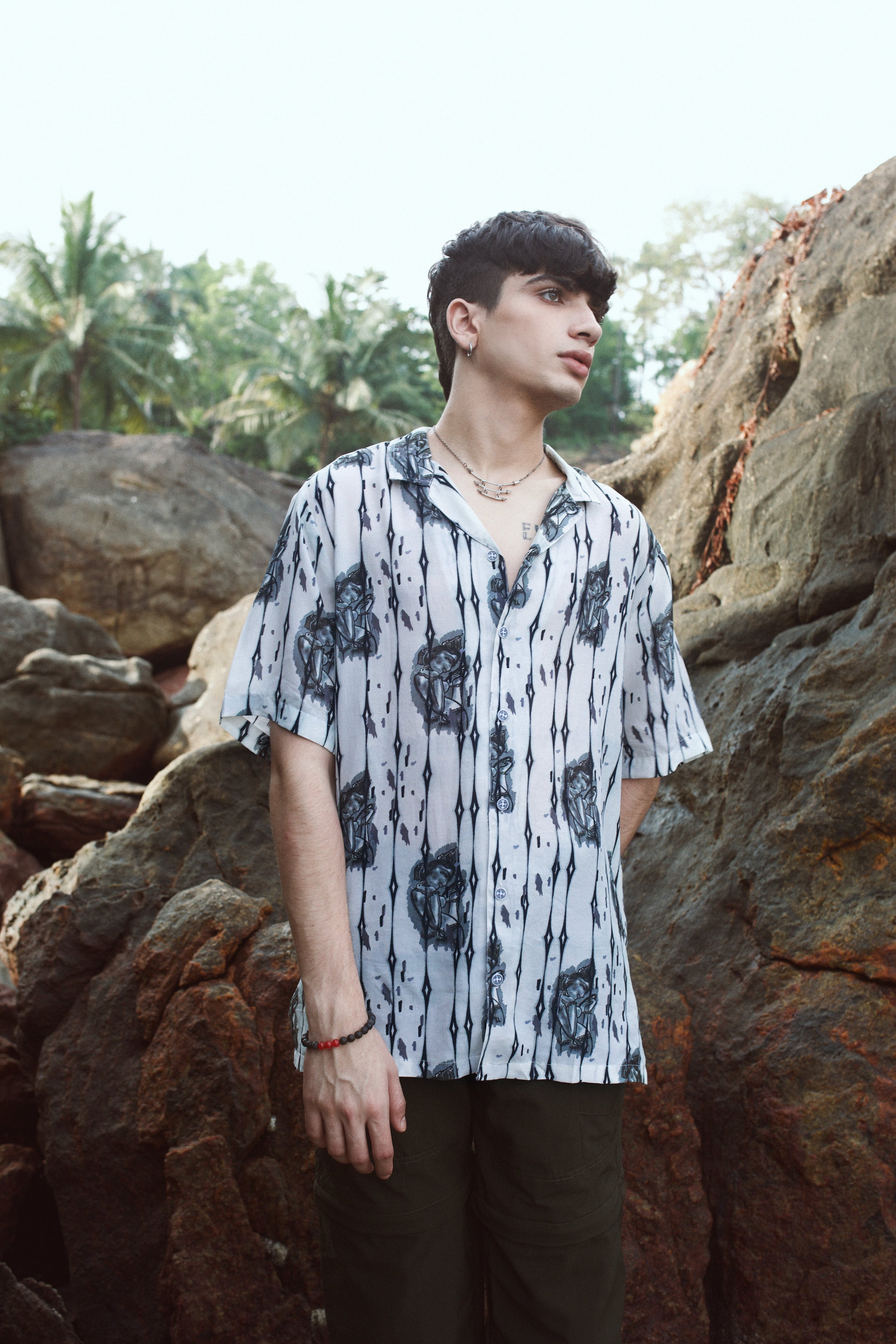 Trendy men's oversized shirt in white with floral patterns, styled outdoors among rocks