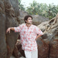 Man wearing a trendy oversized casual shirt against a rocky background with palm trees