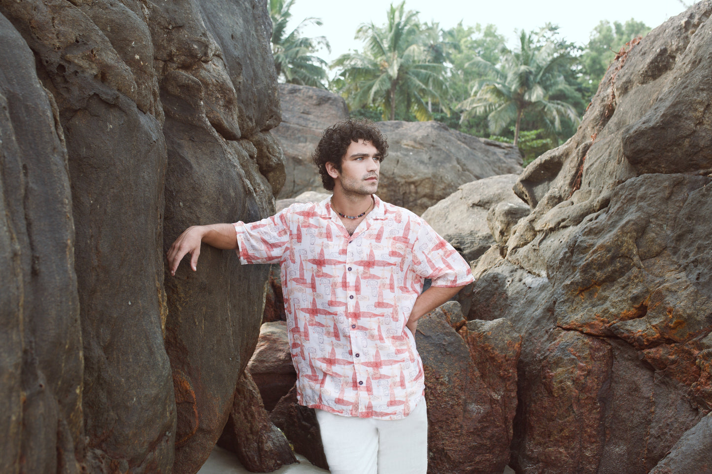 Man wearing a trendy oversized casual shirt against a rocky background with palm trees
